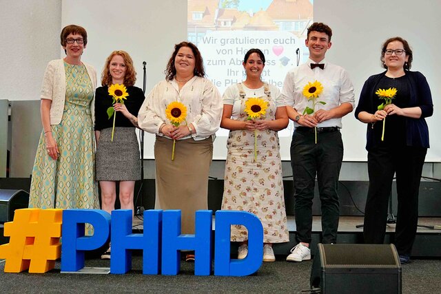 Zu sehen sind Rektorin Vach & Chiara Dold (ganz links, bzw. rechts) sowie 4 Absolvent:innen die für besonderes Engagement mit Sonnenblumen geehrt wurden.