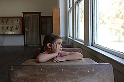 Das Foto zeigt eine Grundschülerin alleine am Tisch in einem leeren Klassenzimmer.