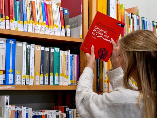 Studentin stellt Buch zurück in das Bücherregal