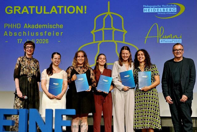 Zu sehen sind Absolvent:innen der PHHD, die sich mit ihren Urkundenmappen auf der Bühne zum Gruppenfoto aufgestellt haben.