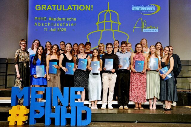 Zu sehen sind Absolvent:innen der PHHD, die sich mit ihren Urkundenmappen auf der Bühne zum Gruppenfoto aufgestellt haben.
