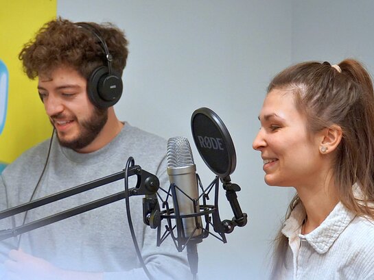 Rechts eine Studentin, links ein Student, sie spricht ins Mikrofon