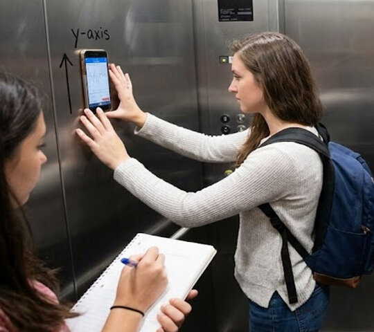 Studierende bei einem Experiment im Fahrstuhl: Mit ihrem Handy messen sie die Geschwindigkeit