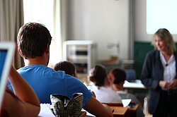 Das Bild zeigt sitzende Studierende an Laptops die eine Lehrende anschauen.
