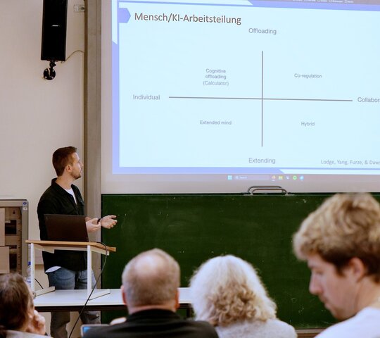Das Foto zeigt einen Redner und Publikum beim Vortrag zu KI-Einsatz in der Lehre 