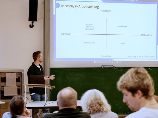 Das Foto zeigt einen Redner und Publikum beim Vortrag zu KI-Einsatz in der Lehre 