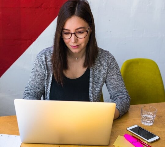 Person sitzt an ihrem Arbeitsplatz und schaut in ein Laptop