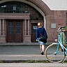 Das Bild zeigt eine junge Frau von hinten. Sie läuft auf das Altbauportal der Hochschule zu. Vorne rechts sieht man ein Fahrrad.