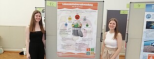 Das Bild zeigt zwei Personen, die vor einem Poster stehen, das sie gerade vorgestellt haben. t.