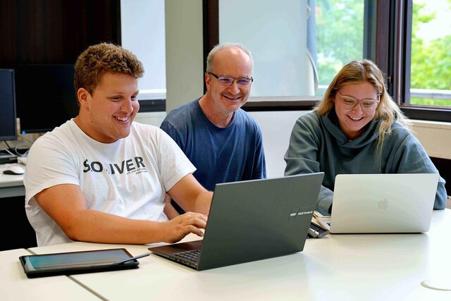 Ein Student, eine Studentin und ein Dozent befinden sich einem Seminar im Lehramtsstudium an der PHHD. Sie alle schauen motiviert und freundlich aus.