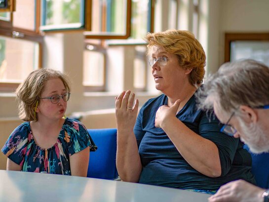 Das Bild zeigt Prof. Dr. Karin Terfloth und Louisa Kabbe. Sie sitzen an einem Tisch, Frau Terfloth spricht und unterstreicht das Gesagte mit ihren Händen. Im Vordergrund ist Hartmut Kabelitz.