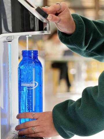 Eine blaue Wasserflasche der PHHD wird in einem Wasserspender mit Sprudelwasser gefüllt