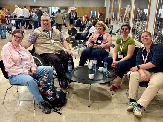 Das Bild zeigt Teilnehmende der Konferenz in der Schweiz. Mehrere Personen sitzen in einem Halbkreis und lächeln in die Kamera.