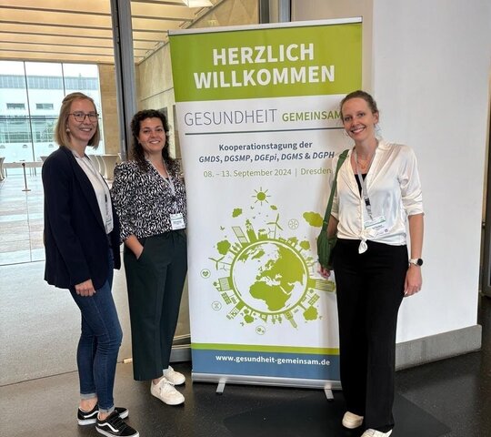 Auf dem Bild sind drei Personen zu sehen, die vor einem Kongress-Poster stehen