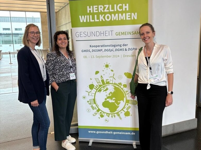 Auf dem Bild sind drei Personen zu sehen, die vor einem Kongress-Poster stehen