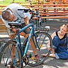 Person repariert Fahrrad, andere Person schaut zu (andere Perspektive)