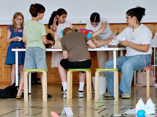 Eine Studentin arbeitete mit verschiedenen Kindern. Sie sitzen gemeinsam um einen Tisch.
