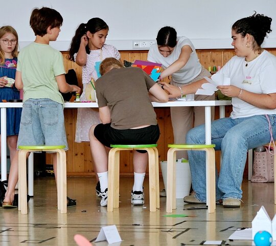 Eine Studentin arbeitete mit verschiedenen Kindern. Sie sitzen gemeinsam um einen Tisch.