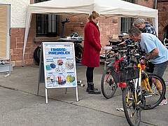 Fahrradreparaturstandeine Person repariert ein Fahrrad. Eine andere Person steht daneben und schaut zu.