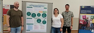 Das Bild zeigt drei Personen, die vor einem Poster stehen, das sie gerade vorgestellt haben.