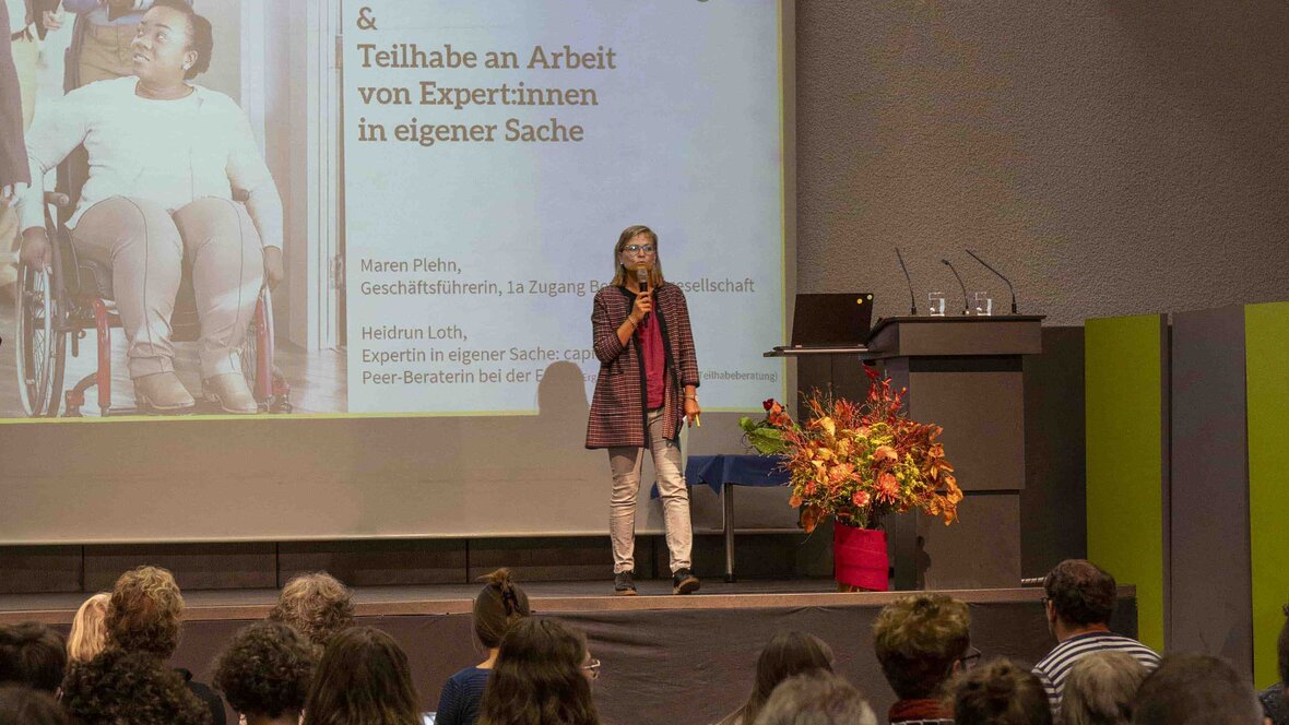 Eine Frau steht auf der Bühne in der Mehrzweckhalle der PH Heidelberg. Sie hält einen Vortrag.