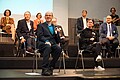 Mehrere Menschen sitzen auf Stühlen oder im Rollstuhl auf der Bühne der Mehrzweckhalle der Pädagogischen Hochschule Heidelberg.