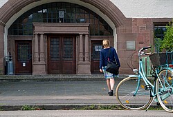 Auf dem Bild erkennt man den Eingang des Altbaus der Ph und einen Studierenden der auf ihn zu läuft.