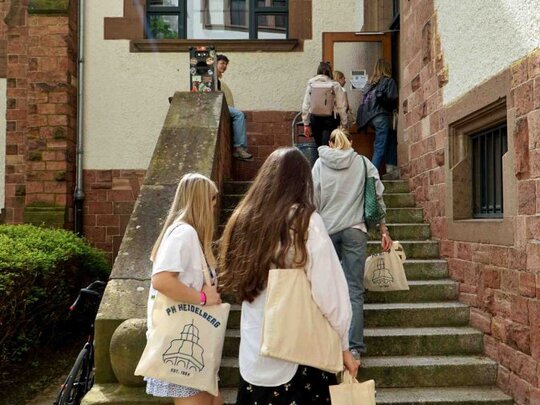 Studierende gehen mit Ihren Taschen in den Altbau der Pädagogischen Hochschule Heidelberg.