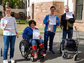 Gruppenbild der Qualifizierungsteilnehmenden: Lilly Lorenz, Maya Silva, Cedric Rueter und Mehmet Can Friedel sind im Innenhof der PH Heidelberg und halten ihre Zertifikate zur bestandenen Modulprüfung in den Händen. Alle lächeln in die Kamera.