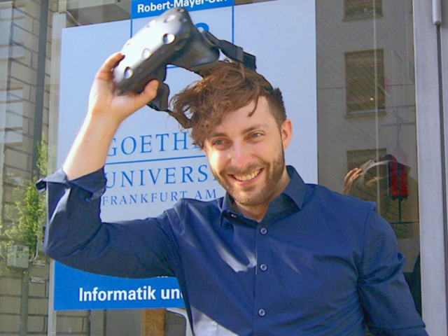 Prof. Dr. Andreas Dengel zieht sich eine VR-Brille vom Kopf, im Hintergrund ein Schild der Goethe-Universität Frankfurt.