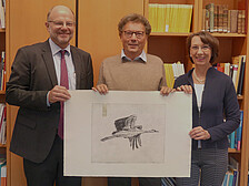 Das Bild zeigt Prof. Friedrich Gervé, der das Preisplakat hält, mit Rektor Prof. Hans-Werner Huneke und Frau Henrike Schön (Leiterin Akademisches Auslandsamt) 