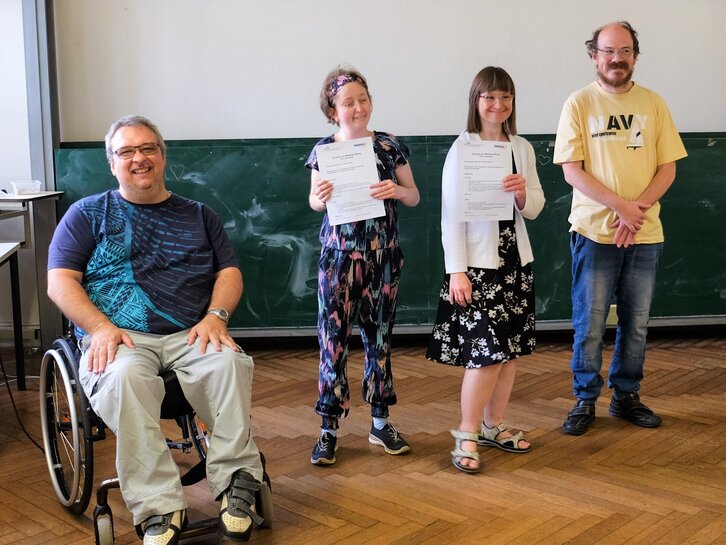 Das Bild zeigt die Qualifzierungsteilnehmerinnen Louisa Kabbe und Susann Bensch nach einer bestandenen Modulprüfung. Sie stehen in einem Seminarraum der Pädagogischen Hochschule Heidelberg, neben den Bildungsfachkräften Helmuth Pflantzer und Thilo Krahnke.