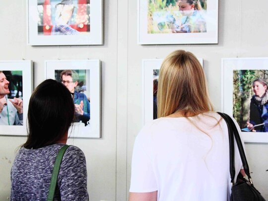 Zwei Frauen betrachten Fotografien, die an einer Wand hängen.