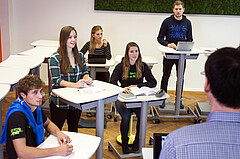 Das Symbolbild zeigt ein Seminar im Stehlabor der Hochschule. Die Studierenden sitzen und stehen verteilt auf den Raum. Copyright: PH Heidelberg.