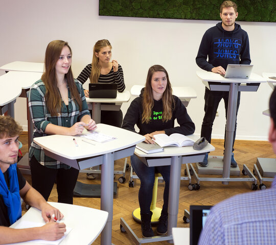 Das Symbolbild zeigt ein Seminar im Stehlabor der Hochschule. Die Studierenden sitzen und stehen verteilt auf den Raum. Copyright: PH Heidelberg.