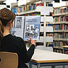 Auf dem Bild sieht man eine Frau von hinten. Sie sitzt in der Bibliothek der Hochschule und liest den Jahresbericht. 
