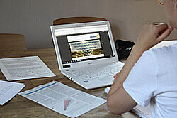Das Bild zeigt eine Person an einem Schreibtisch mit aufgeklapptem Laptop und Papierzettel daneben. Copyright Pädagogische Hochschule Heidelberg