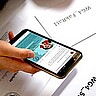 Das Bild zeigt eine Hand, die ein Smartphone in der Hand hält. Im Hintergrund sind Wahlunterlagen zu sehen.