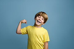 Das Symbolbild zeigt einen Junge, der breit lächelt und seine rechts Faust hebt. 