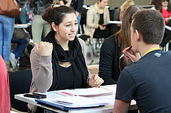 zwei Studierende die sich gegenüber sitzen und sich unterhalten.