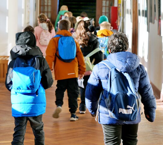 Kinder mit Rucksäcken und Jacken rennen über einen Gang
