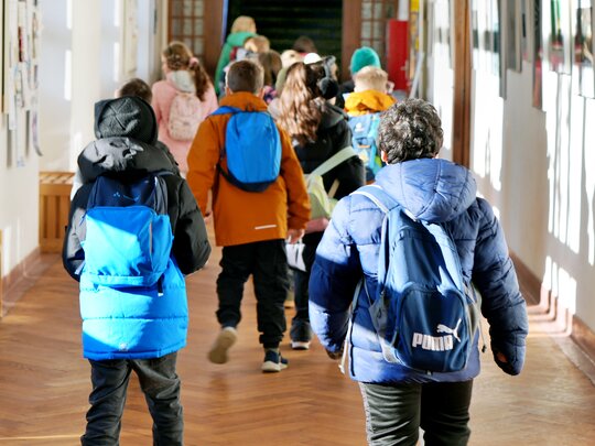 Kinder mit Rucksäcken und Jacken rennen über einen Gang