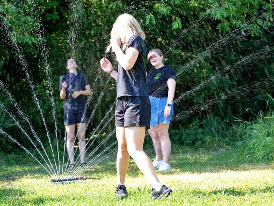 Zu sehen sind drei Frauen und ein Regensprenger im Ökogarten