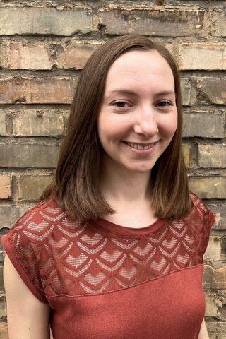 Zu sehen ist ein Protraitfoto von Alumna Ronja Schneider vor einer Ziegelwand.