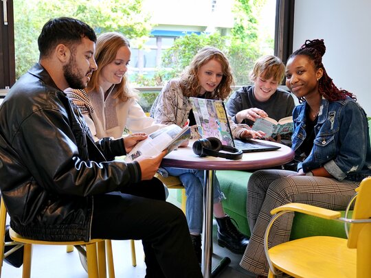 Das Foto zeigt verschiedene Studierende an einem Tisch sitzend.