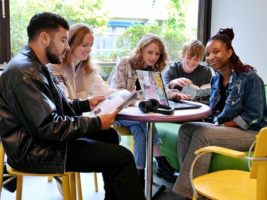 Das Foto zeigt verschiedene Studierende an einem Tisch sitzend.
