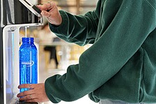 Detailaufnahme wie sich jemand im Neubau Wasser aus dem Wasserspender zieht