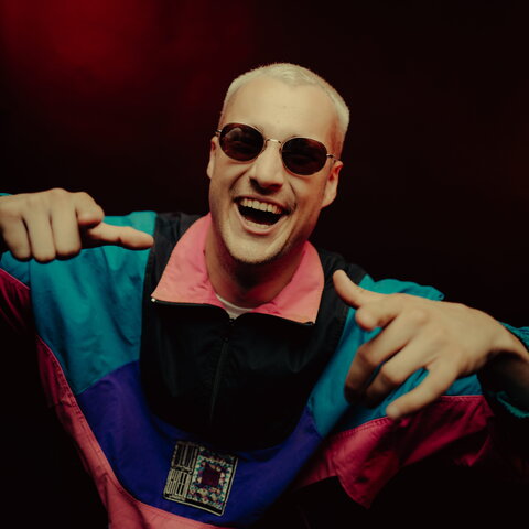 Porträtfoto von Paul Keen. Er trägt eine bunte Trainigsjacke und eine Sonnenbrille.