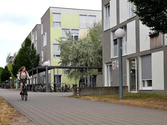 Zu sehen sind Wohnheime der Studierendenstadt Heidelberg und eine Studentin die auf dem Fahrrad zur Pädagogischen Hochschule Heidelberg fährt.