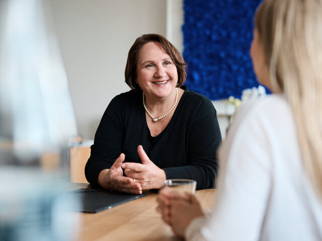Ministerin Theresa Schopper im Gespräch mit einer Frau, die man von hinten sieht. Schopper redet deutlich mit den Händen.